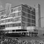 Blick auf das fünfstöckige Verwaltungsgebäude in Kork, davor wehen Fahnen und ein Fußgängerüberweg ist zu sehen, das Foto ist schwarz-weiß