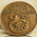 eine bronzene Plakette mit der Aufschrift Ehrenplakette der Stadt Radeberg, darunter das Wappen der Stadt, ein Löwe auf einem alten Holzrad
