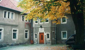 Blick in den Hof der Tobiasmühle, ein altes graues Gebäude, im Innenhof steht ein Baum, dessen Blätter gelb gefärbt sind