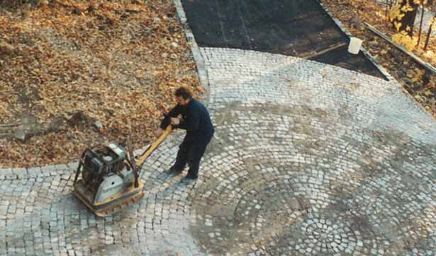 Ein Mann mit einer Rüttelplatte verdichtet das Granitpflaster