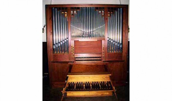 Die neue Orgel, sie besticht durch kirschrotes Holz, davor steht eine Bank