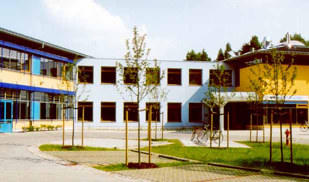 Blick auf drei Gebäude mit blau-gelber Fassade, davor eine große Freifläche