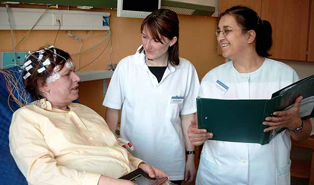 zwei Krankenschwestern stehen an dem Patientenbett, die Patientin ist an einem EEG angeschlossen