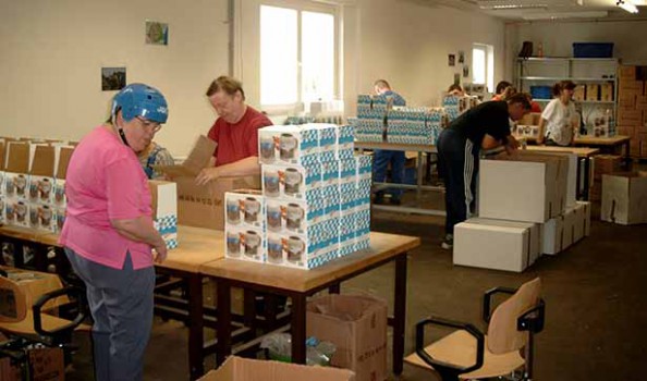 mehrere Beschäftigte verpacken Bierkrüge in Kartons