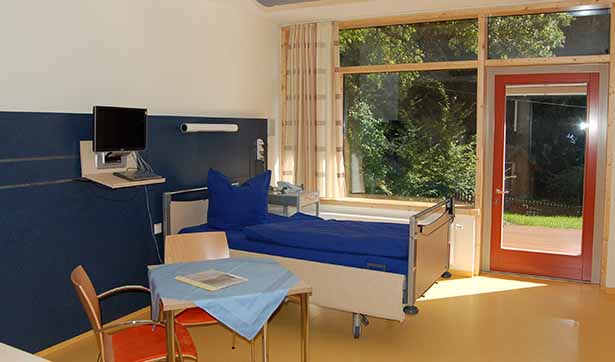 Ein helles, lichtdurchflutetes Zimmer mit einem Patientenbett und Tisch und Stühlen