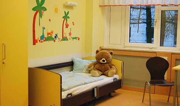 Blick in ein Zimmer der Kinderstation, auf einem Bett sitzt ein Plüschbär