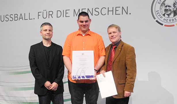 Der Fußballspieler des FC Kleinwachau, Roman Eichler, hält die Urkunde in der Hand. Daneben stehen der Trainer Lutz Höhne und der Vereinspräsident Markus Rebs